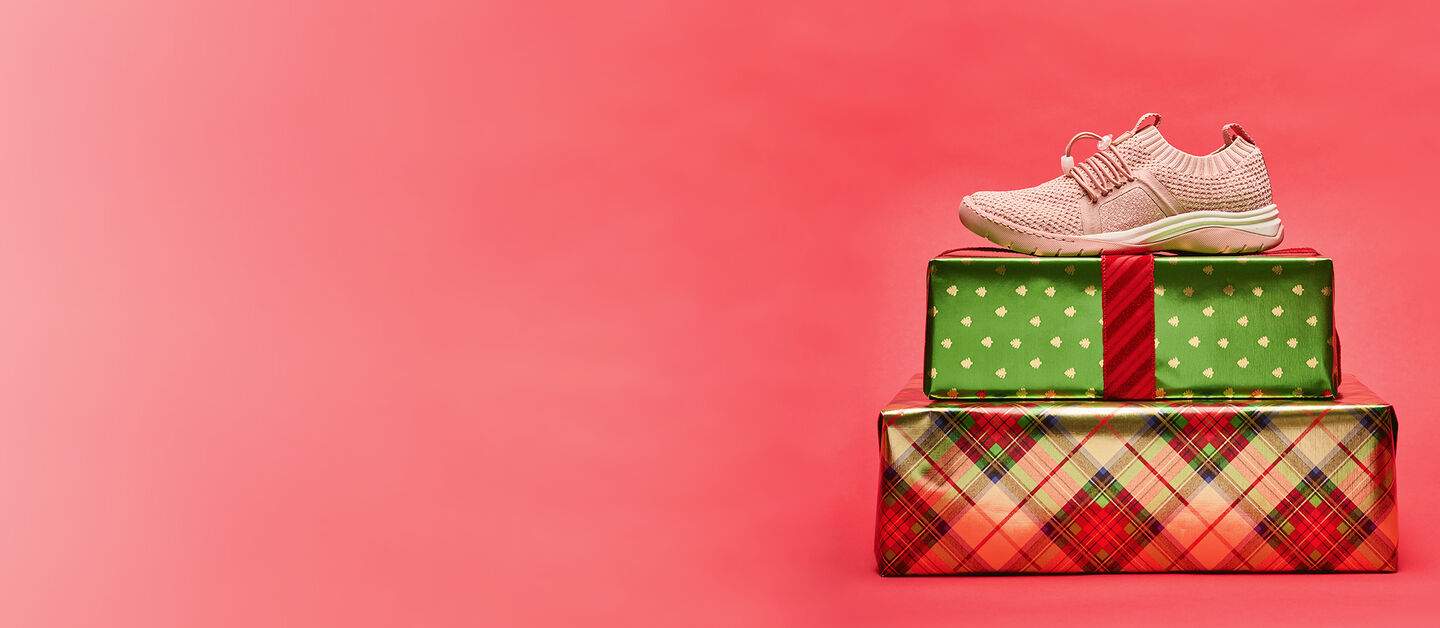 Imagen de Torri en Dusty Rose, foto de perfil, encima de dos regalos de Navidad sobre un fondo rojo.